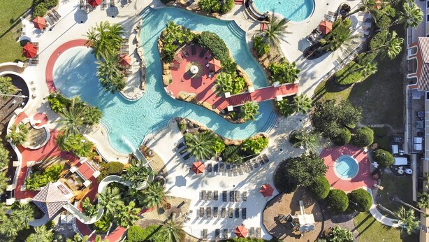 Vista aérea de un complejo turístico con varias piscinas, tumbonas y palmeras.