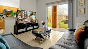 Una sala de estar moderna con una mesa de centro de vidrio, un sofá negro y un televisor de pantalla plana sobre un mueble negro.