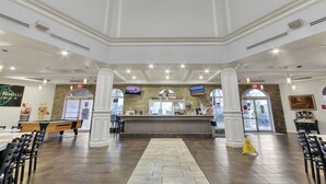 Un vestíbulo amplio con una zona de bar central, diversas opciones de asientos y vistas al acceso exterior.