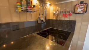 Een keuken met een zwart aanrecht, een fornuis en diverse keukengerei aan de wand.