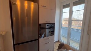 Een kleine keuken met een roestvrijstalen koelkast, een inbouwoven en een raam met uitzicht.