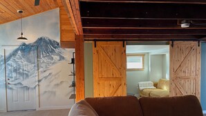 Ein gemütliches Wohnzimmer mit einer großen Couch, Holzwänden, einer Bergmalerei und einer Schiebetür im Bauernhausstil.