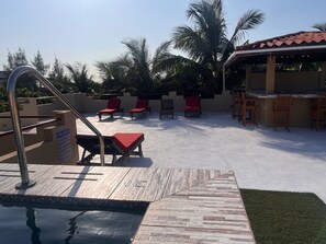Uma área de piscina com um deck revestido, espreguiçadeiras e um bar.