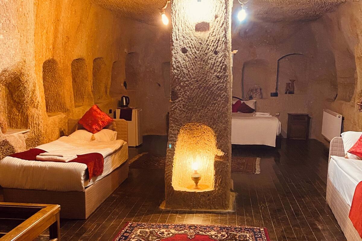 A room with a stone wall, a central pillar with a light, a bed with a red pillow, a sofa, and a patterned rug.