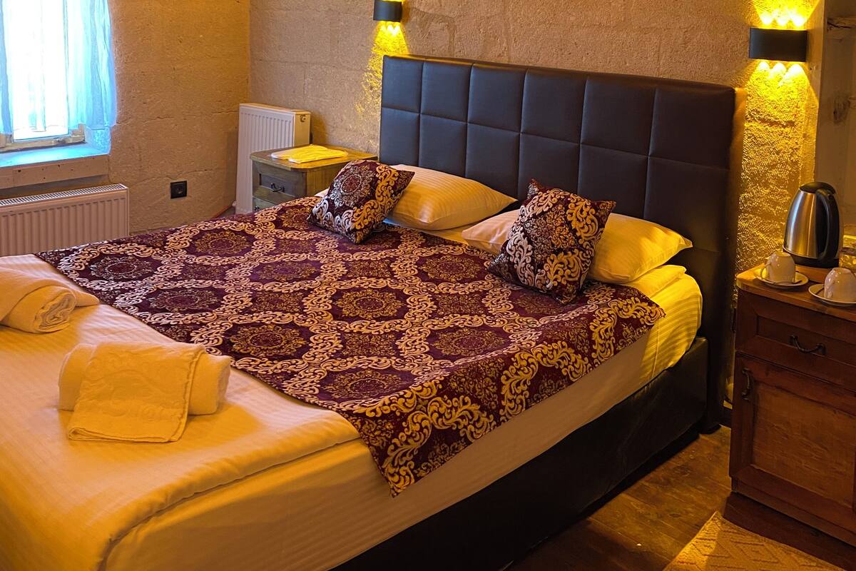 A bedroom with a large bed, a nightstand, a dresser, and a wall-mounted light fixture.