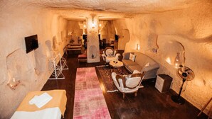 A cozy, cave-like interior with a sofa, chairs, a small table, and a fan. - 7 Oda Kapadokya Cave House (Urgup)