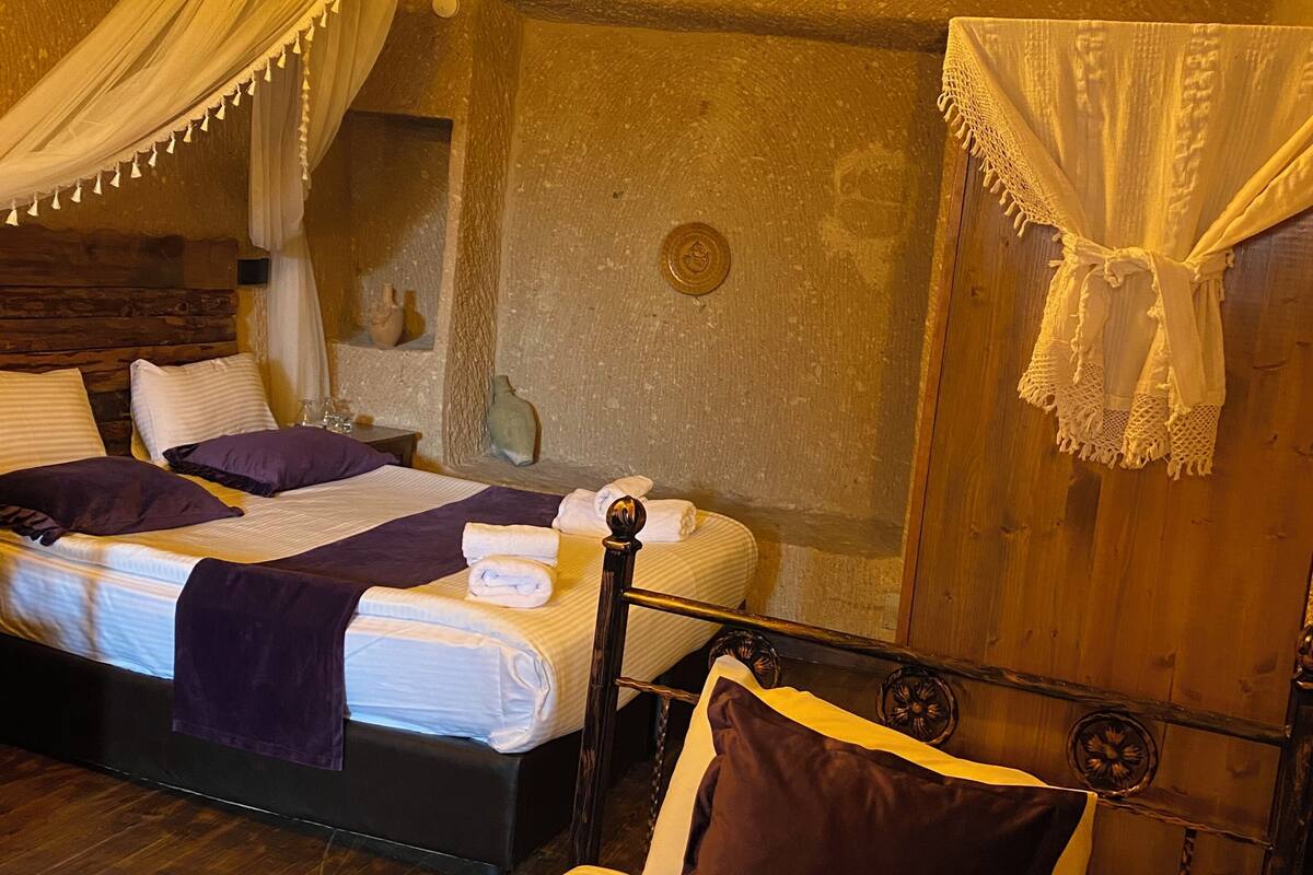 A room with two beds, a wooden headboard, a canopy bed, a chandelier, and a wall-mounted clock.