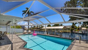 A swimming pool with a pink flamingo float, surrounded by lounge chairs and a covered area with a view of the water.