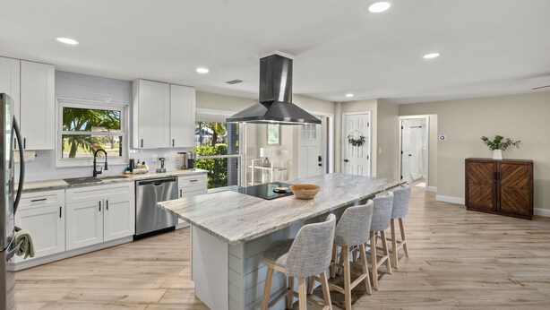 A modern kitchen with white cabinets, a central island with bar stools, a stainless steel dishwasher, and a large range hood.