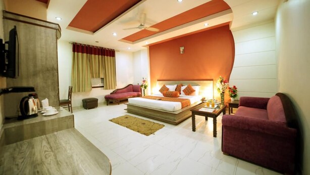 A modern hotel room with a large bed, a sofa, a coffee table, and a TV. - Hotel Blue Bell (New Delhi)