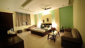 A hotel room with a bed, a sofa, a coffee table, a TV, and a ceiling fan. - Hotel Blue Bell (New Delhi)