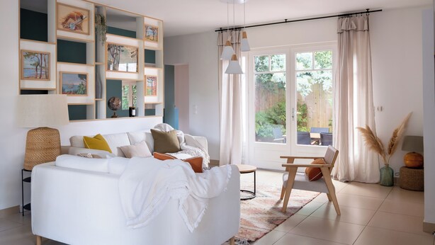 Una sala de estar moderna con un sofá blanco, una mesa de comedor y un amplio ventanal con cortinas.
