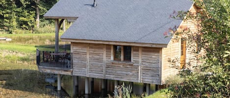 A wooden cabin with a balcony, situated by a body of water, surrounded by greenery.