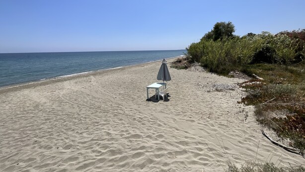 Ein Strand mit Tisch und Sonnenschirm, bewölkter Himmel und ruhiges Meer.