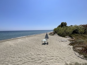 A beach with a table and umbrella, clear sky, and calm sea.
