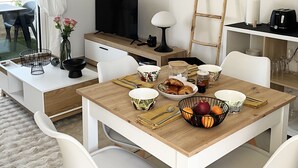 Ein modernes, helles Zimmer mit einem Holzespeisetisch, der für das Frühstück gedeckt ist, einem Fernseher und einem Spiegel an der Wand.
