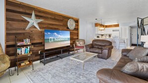 Una sala de estar con pared de madera, una decoración con forma de estrella, un reloj, un televisor, un sofá, una mesita de centro y una estantería.