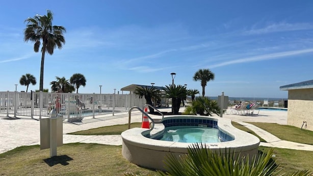 Un área de piscina con jacuzzi, palmeras y sillas de descanso.