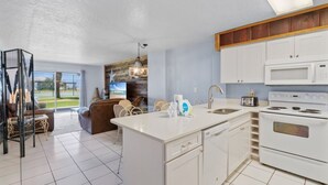 Una cocina moderna con armarios blancos, microondas integrado y estufa. Hay un comedor con un sofá marrón y una araña.