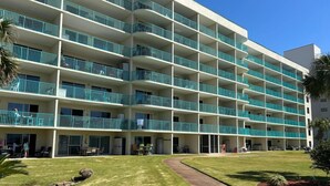 Un hotel de varios pisos con balcones, un césped cuidado y un camino que lleva a la entrada.