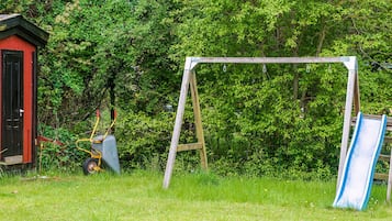 A playground with a swing set and a slide, surrounded by greenery.