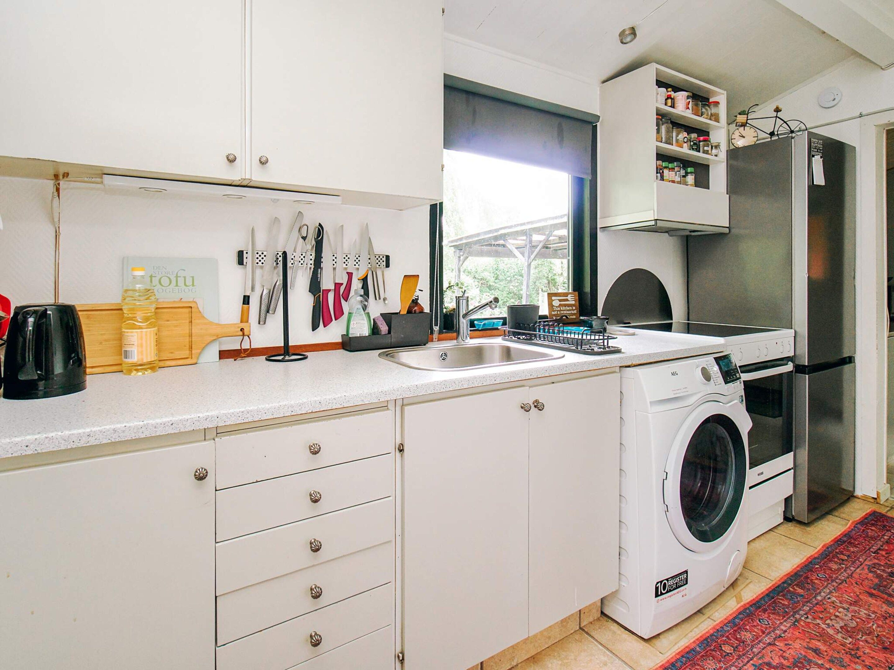 A compact kitchen with a built-in washing machine, a sink, and a window providing natural light.