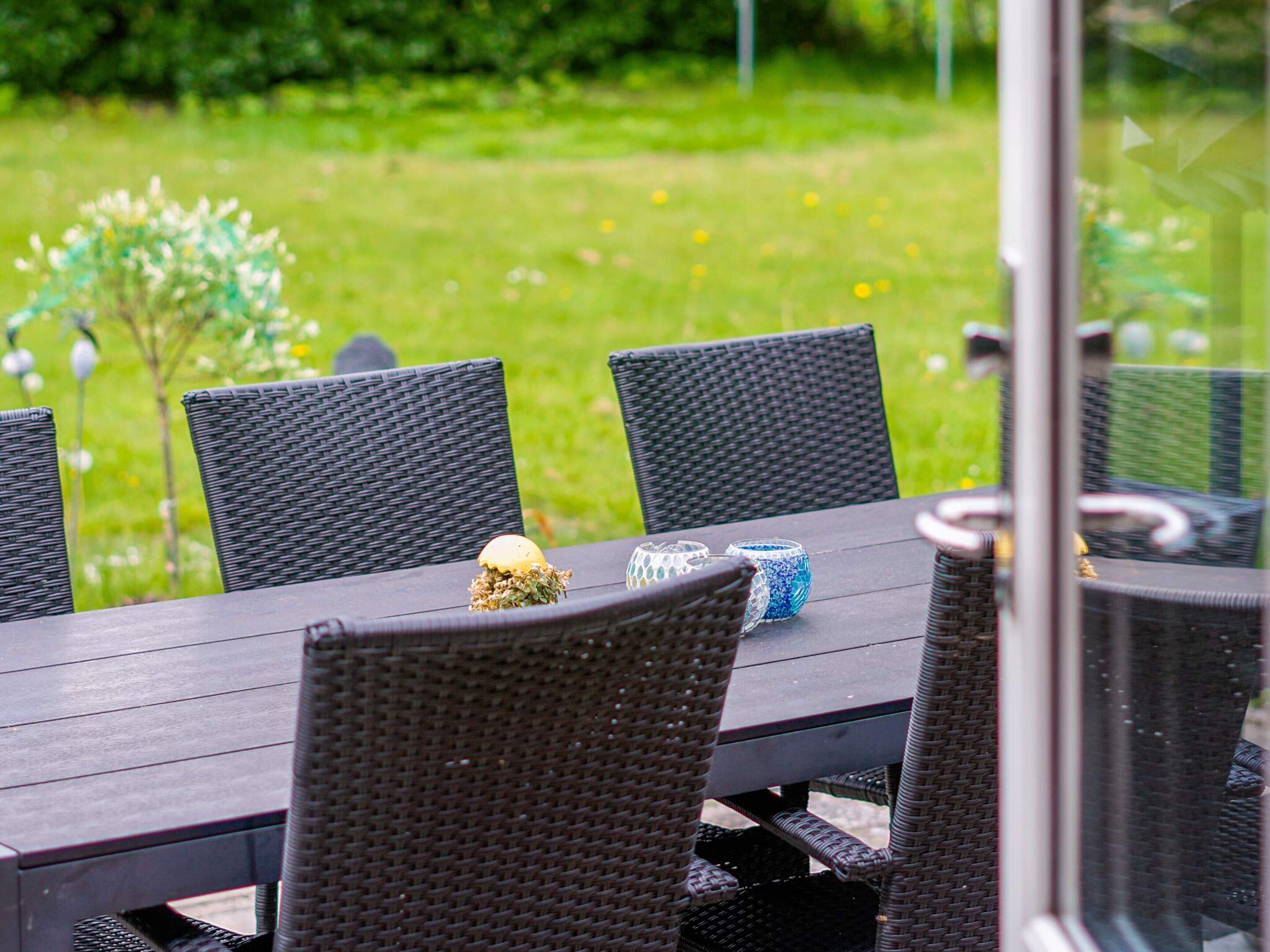 An outdoor dining area with wicker chairs and a table, set against a grassy background.