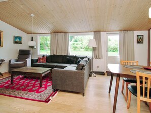 A cozy living room with a sofa, armchair, coffee table, and dining table. There are windows with curtains, a lamp, and artwork on the walls. - 8 Person Holiday Home in Holbaek (Holbaek)