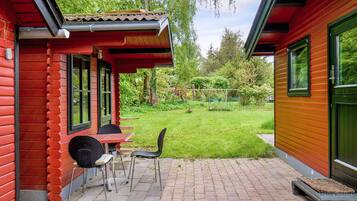 A red wooden house with a patio area featuring a table and chairs.