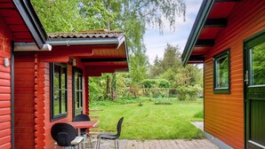 A red wooden house with a patio area featuring a table and chairs, surrounded by a well-maintained garden. - 8 Person Holiday Home in Holbaek (Holbaek)