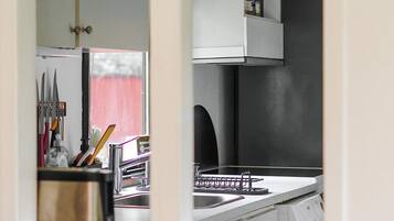 A kitchen with a sink, a dish rack, and a window with a red curtain.
