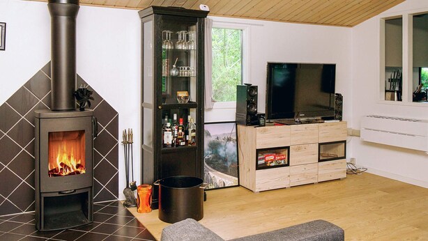 A living room with a wood-burning stove, a glass cabinet with bottles, a television, and a wooden cabinet. - 8 Person Holiday Home in Holbaek (Holbaek)