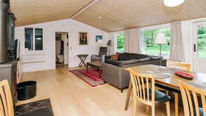 A spacious living area with a wooden ceiling, a grey sofa, a dining table with chairs, and a view of greenery outside. - 8 Person Holiday Home in Holbaek (Holbaek)