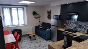 Un espace de vie compact comprenant un coin cuisine, un canapé, une table à manger avec des chaises et une fenêtre avec des rideaux.