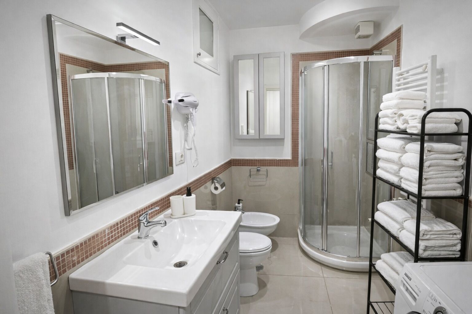 A modern bathroom with a large mirror, a white sink, a toilet, a glass shower enclosure, and a towel rack with neatly folded towels.