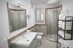 Ein modernes Badezimmer mit einem großen Spiegel, einem weißen Waschbecken, einer Toilette, einer Duschkabine aus Glas und einem Handtuchhalter mit ordentlich gefalteten Handtüchern.