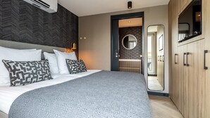 Une chambre d’hôtel moderne dotée d’un grand lit, d’une armoire intégrée, d’un miroir et d’une salle de bain avec un meuble-lavabo et un évier.