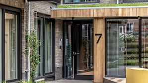Une entrée moderne avec une porte en verre, un pilier en bois portant le numéro 7 et un petit espace extérieur aménagé en coin salon.