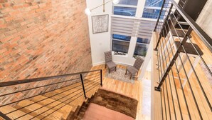 A staircase leading to a loft bedroom with a brick wall, a large window, and a view of the sky.