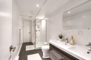 A modern bathroom with a glass shower enclosure, a white toilet, a vanity with a mirror, and a sink.