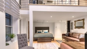 A modern bedroom with a large bed, a grey armchair, a brown sofa, and a small table.