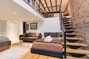 Ein Schlafzimmer im Loft-Stil mit einer Holztreppe, einem Sofa, einem Bett und einem großen Spiegel.