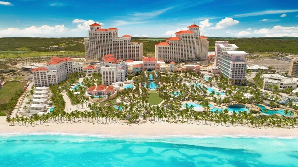 Un resort con varias edificaciones, un área de piscina central y una playa.