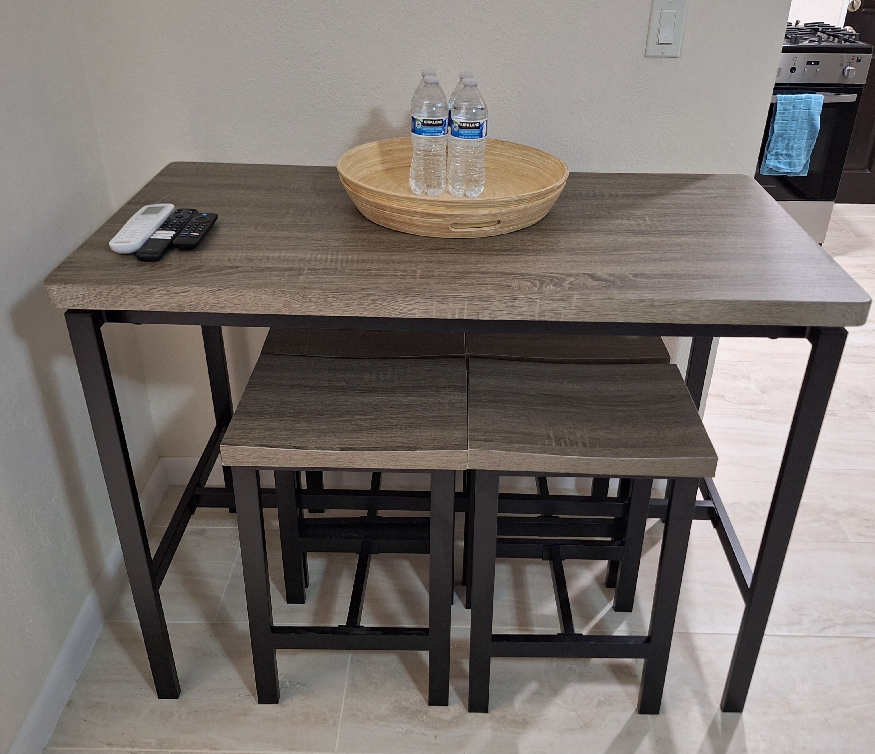 Une table à manger avec un plateau en bois et des pieds en métal noir, accompagnée d’un plateau sur lequel se trouvent deux bouteilles d’eau.