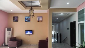 A lobby with a TV, two sofas, artwork on the walls, and a ceiling light fixture. - HOTEL SYLVIA (Enugu)
