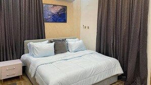 A bedroom with a bed, a nightstand, a wall-mounted air conditioner, and a painting. - HOTEL SYLVIA (Enugu)