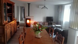 A dining area with a wooden table, chairs, a vase with flowers, a television, and a fireplace.