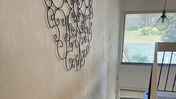 Una escalera con alfombra marrón, un adorno de pared y una ventana con persianas.
