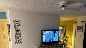 Una sala de estar con un sofá, un televisor, un ventilador de techo y un elemento decorativo en la pared.