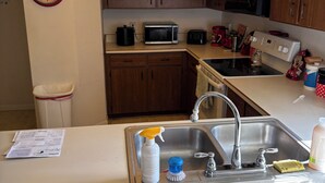 Cocina con gabinetes de madera, microondas, tostadora y lavabo con productos de limpieza.
